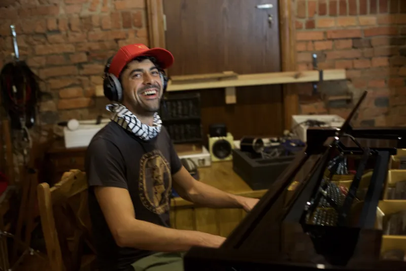 Leo Lazar lachend am Klavier, mit Kopfhörern und rotem Tuch um den Hals